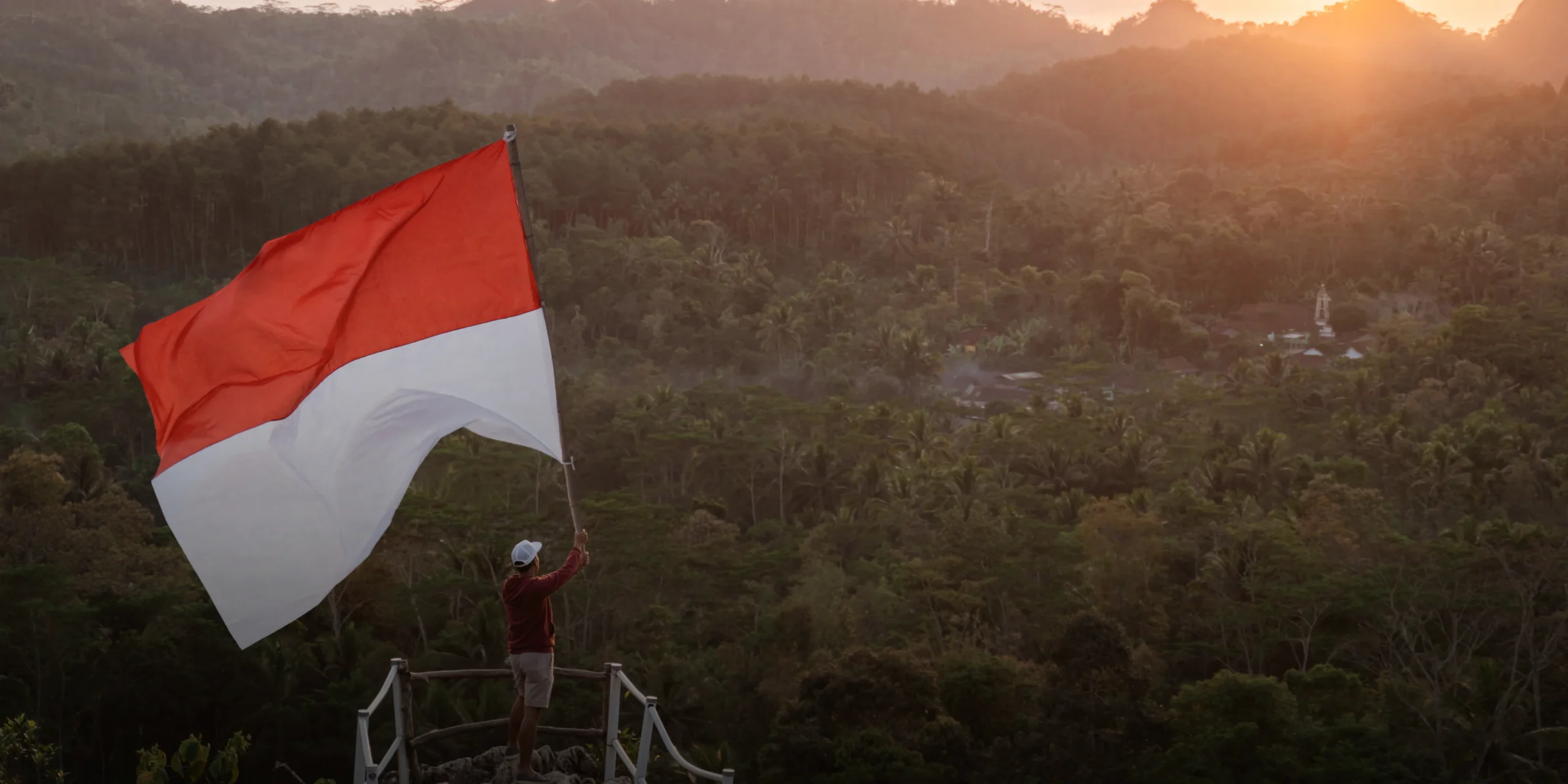 A man waving an Indonesia flag on top of a mountain representing Indonesia and its trademark registration system | KASS Malaysia Indonesia